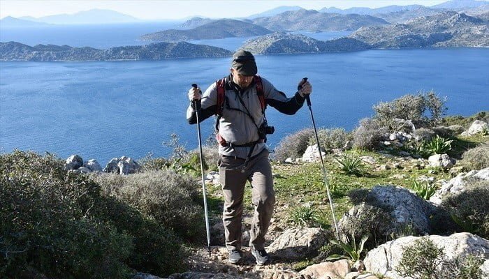 Karia Yolu’nda deniz manzarası eşliğinde batonlarla yürüyen erkek