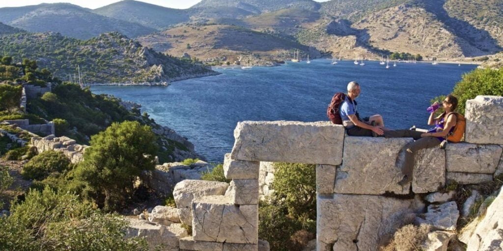Karia Yolu antik taş kalıntılarında deniz manzarasına karşı mola veren yürüyüşçüler