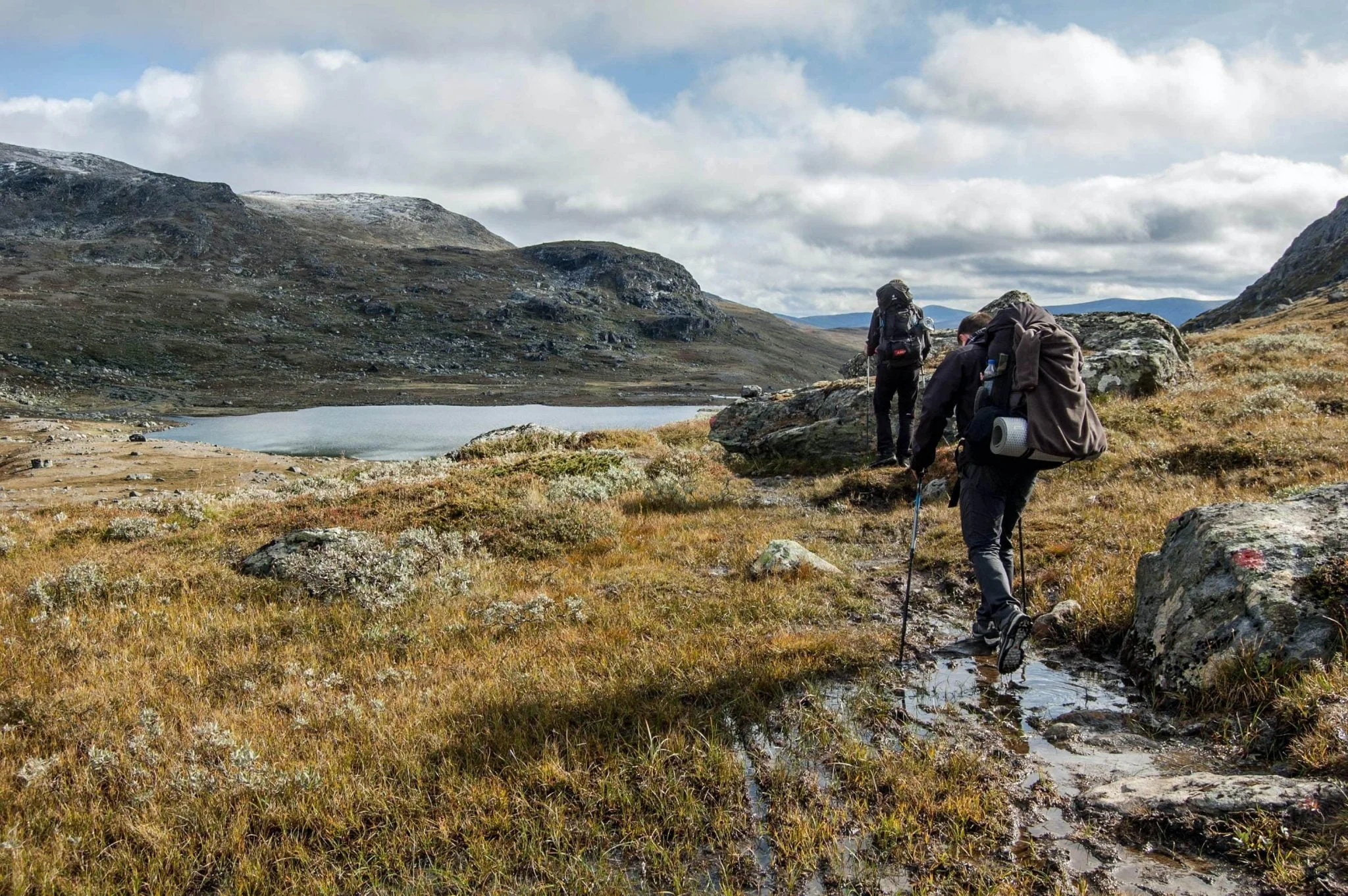 Dağ gölü kıyısında batonlarla trekking yapan iki yürüyüşçü